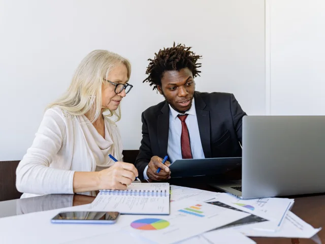 A technology professional reviewing business reports with a client beside a laptop